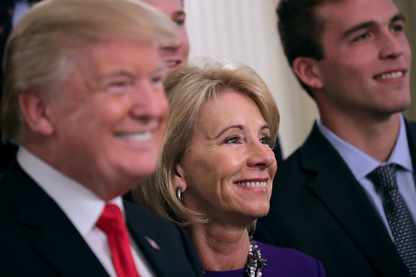 WASHINGTON, DC - NOVEMBER 17: (AFP OUT) U.S. President Donald Trump and Education Secretary Betsy Devos pose for photographs with members of the National Collegiate Athletic Association's champion University of Virginia men's tennis team in the East Room of the White House November 17, 2017 in Washington, DC. The White House welcomed athletes representing universities and colleges from across the country to meet Trump who congratulated them on their NCAA victories in sports like lacrosse, bowling, gymnastics, golf, rowing and others.